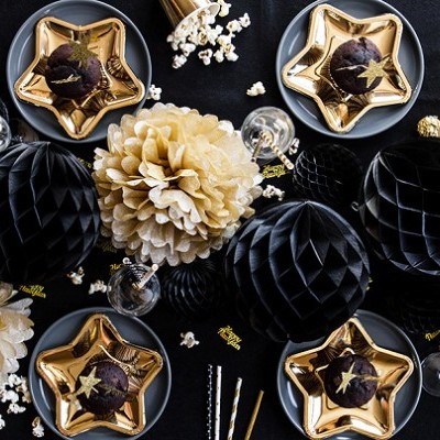 Decoração festiva com pratos dourados em forma de estrela, bolinhos de chocolate, flores creme de papel, balões pretos de papel e pipoca