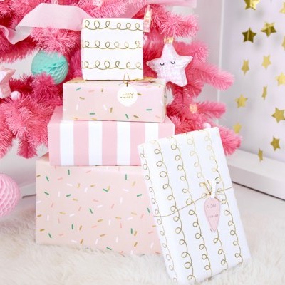 Caixas de presente coloridas junto a árvore de Natal rosa com decoração e fundo estrelado