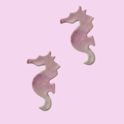 Brincos em forma de cavalos-marinhos em tons rosa e branco sobre fundo rosa