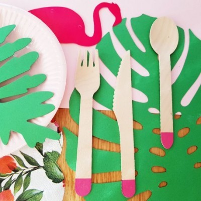 Talheres de madeira com ponta rosa sobre individual verde de folhas com prato branco e guardanapo floral