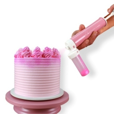 Bolo rosa com decoração em chantilly e suporte rosa, mão a segurar aplicador de cobertura.