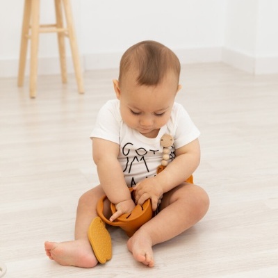 Bebé sentado no chão a brincar com brinquedo laranja partido