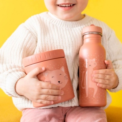 Criança com camisola branca segura garrafa e recipiente rosa com desenhos de gatos.