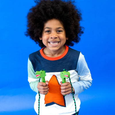 Criança sorridente com camisola colorida e brinquedos de dinossauro em fundo azul