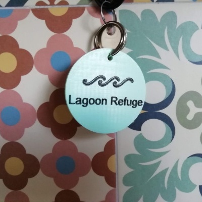 Chaveiro azul claro com ondas e texto 'Lagoon Refuge' num fundo colorido