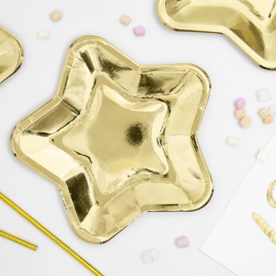 Pratos descartáveis dourados em formato de estrela sobre superfície branca com confetes e apitos dourados