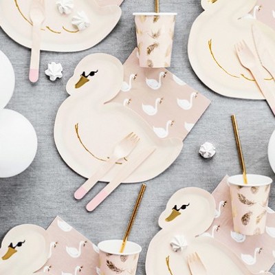Artigos de festa com tema de cisne, pratos, copos, guardanapos e talheres sobre mesa cinza