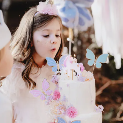 Menina a soprar vela em bolo branco decorado com borboletas e flores