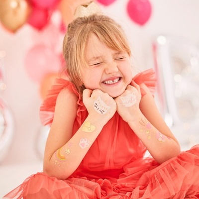 Menina sorridente com vestido vermelho e tatuagens temporárias em ambiente festivo com balões