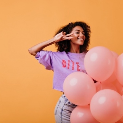 Mulher com camisola lilás e balões cor-de-rosa num fundo laranja