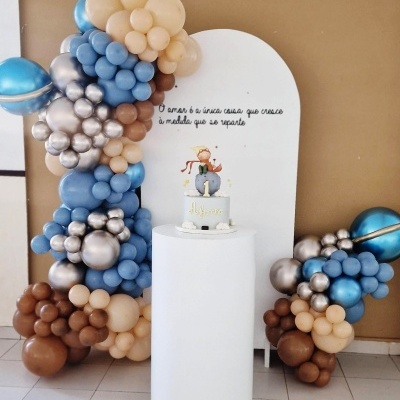 Painel branco com texto e bolos decorado com balões coloridos numa parede castanha