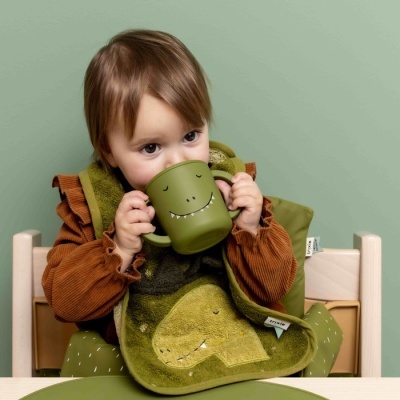 Copo e babete de dinossauro verde usados por criança sentada