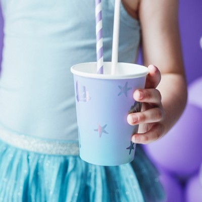 Criança segurando copo azul claro com estrelas do mar e canudos, em fundo com balões lilás