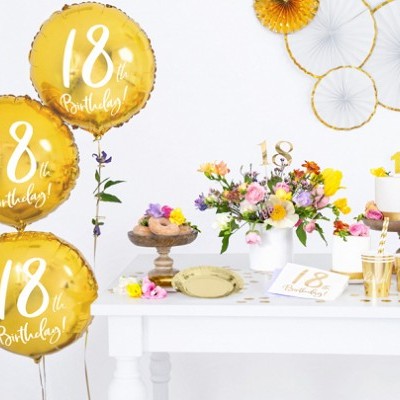 Decoração de festa de 18 anos com balões dourados, flores, bolos e acessórios em branco e dourado