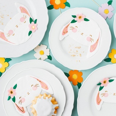 Pratos brancos com desenhos de coelhos rosa em superfície azul com flores