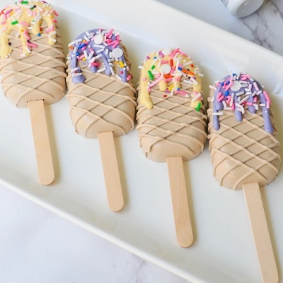 Quatro gelados decorativos com cobertura colorida e granulados, em prato branco.