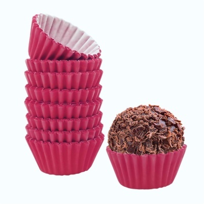 Forminhas cor-de-rosa para brigadeiro empilhadas próximas a brigadeiro coberto com raspas em suporte cor-de-rosa.