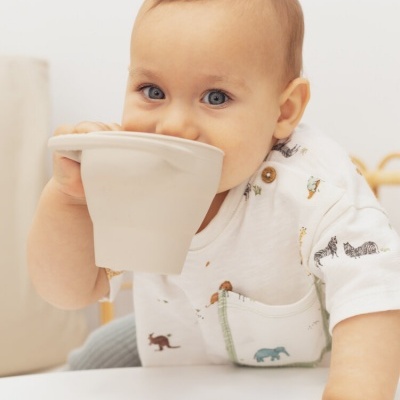 Bebé com camisa branca estampada segura taça branca.