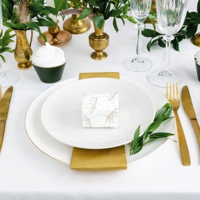 Mesa posta com prato branco, talheres dourados e decoração verde
