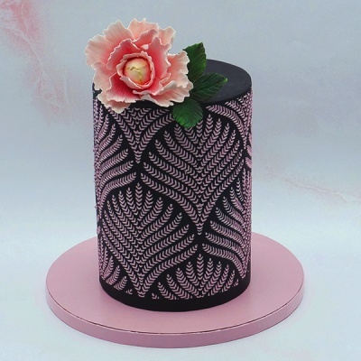 bolo cylindrical preto com padrão rosa e flor decorativa no topo