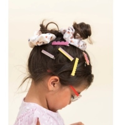 Criança com scrunchies e ganchos de cabelo coloridos em cabelo castanho preso em coques, de perfil.