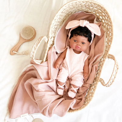 Boneca de bebé em cesta de verga com tecido rosa e escova de cabelo de madeira