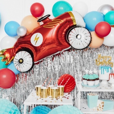 Decoração de festa com balões coloridos, balão carrinho vermelho, bolo e cupcakes em fundo prateado.