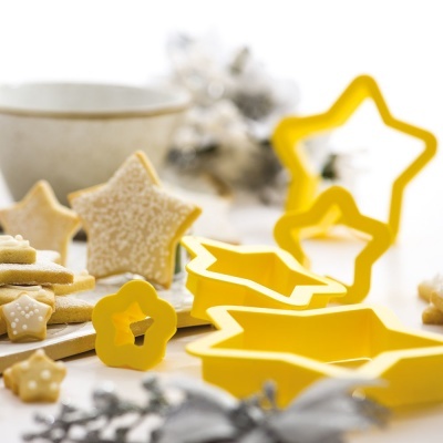 Conjunto amarelo de cortadores de bolachas em forma de estrela e flor, bolachas decoradas e chávena branca ao fundo