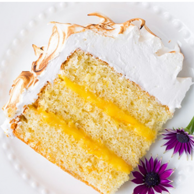 Fatias de bolo amarelo com recheio cremoso e cobertura branca, decoradas com flores roxas