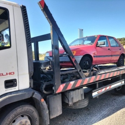 Camião de reboque branco a transportar um carro vermelho em estrada sob céu azul
