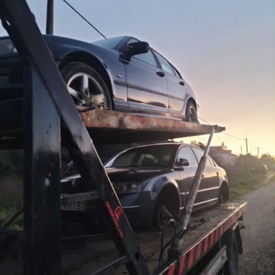 Dois carros cinzentos-escuros em um reboque preto com detalhes vermelhos ao entardecer