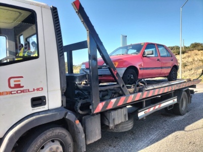 Camião de reboque branco a transportar um carro vermelho em estrada sob céu azul
