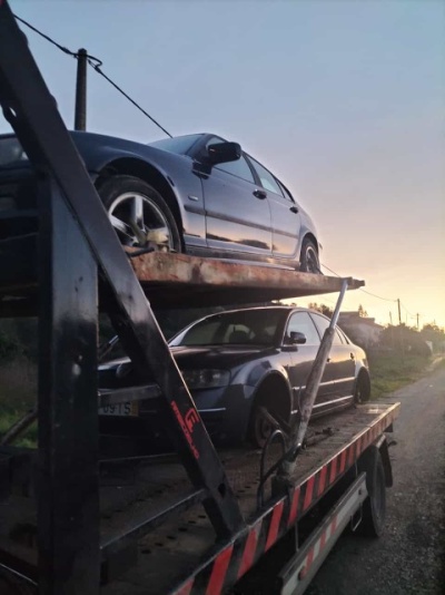 Dois carros cinzentos-escuros em um reboque preto com detalhes vermelhos ao entardecer