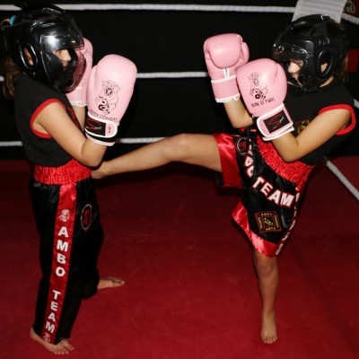 Dois jovens a treinar boxe com capacetes e luvas rosas em ringue.