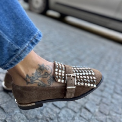 Sapato mocassim castanho com tachas e fivela em camurça, usado com calças de ganga azuis na rua