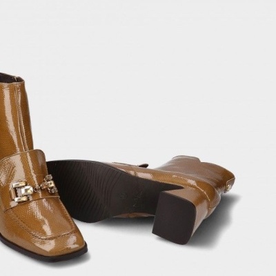 Botas castanhas brilhantes com salto quadrado e detalhe dourado no fundo cinzento