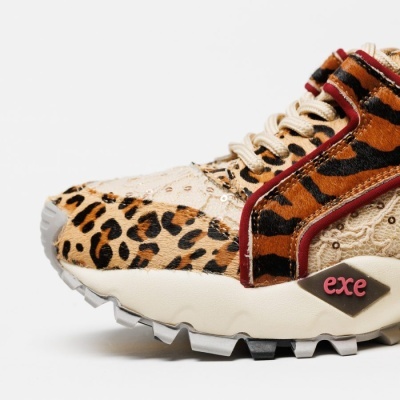 Tênis desportivo com padrão animal print em tons castanhos, bege e preto, com detalhes vermelhos e sola branca.