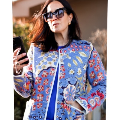 Mulher com casaco azul floral e óculos de sol a segurar telemóvel