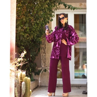 Mulher com fato bordeaux e padrão floral com óculos e plataforma numa entrada com plantas