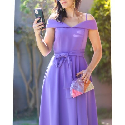 Mulher com vestido longo lilás e carteira colorida ao ar livre