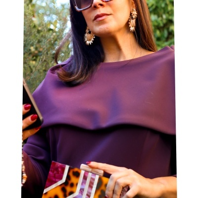 Mulher com vestido roxo, brincos dourados, óculos de sol e carteira de mão padrão animal print
