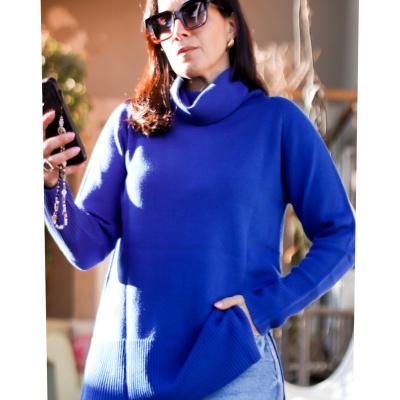 Mulher com camisola de gola alta azul e calças de ganga claras a segurar telemóvel