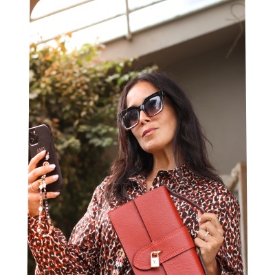 Mulher com mala vermelha, blusa animal print e óculos de sol.