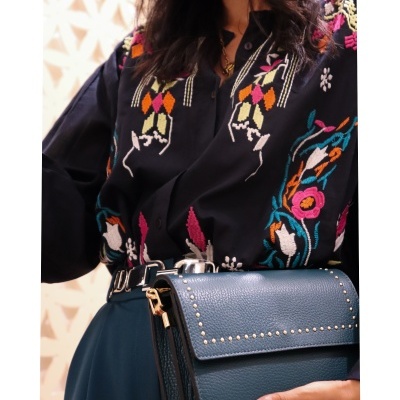 Mulher com blusa preta bordada colorida e bolsa preta com tachas