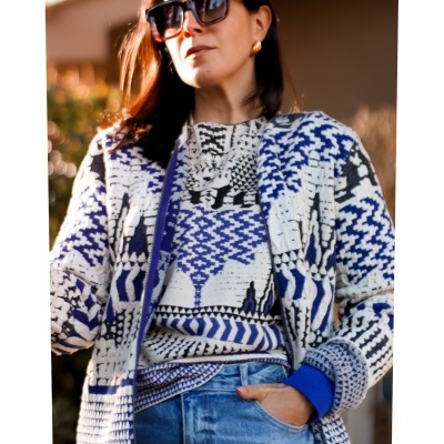 Mulher com casaco de malha colorido, camiseta e jeans azuis, usando óculos de sol