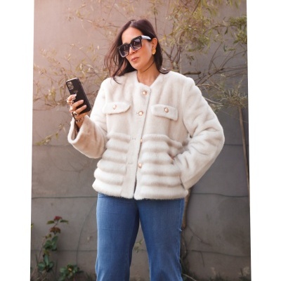 Mulher com casaco felpudo branco e calças azuis ao ar livre