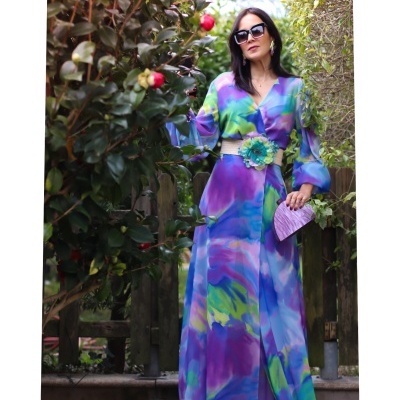 Vestido longo colorido fluido com cinto florido, óculos escuros e mala lilás num jardim
