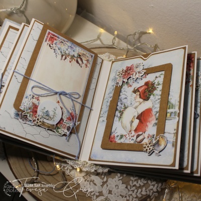 Álbum aberto com decoração em papel kraft e branco, ilustração de mulher com gorro vermelho, flores de papel e fita azul em ambiente decorado com luzes e tecido floral.