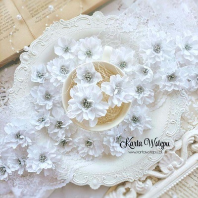 Flores artificiais brancas de tecido com detalhes cinzentos no centro sobre superfície rendada branca e prato decorativo branco