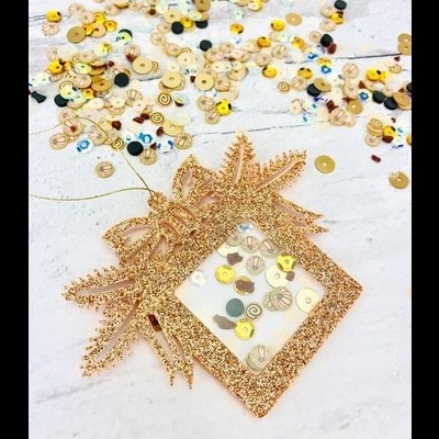 Moldura decorativa em glitter dourado com lantejoulas coloridas e laço, sobre fundo branco com lantejoulas espalhadas.